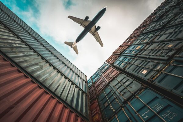 Freight airplane flying above overseas shipping containers.
