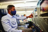 A man wearing a mask scrolls through the Delta Studio selections on the IFE in Main Cabin during COVID